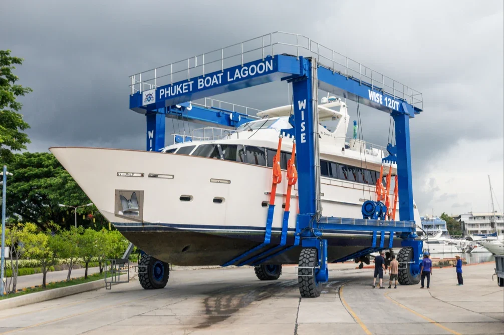Мобильный подъёмник Phuket Boat Lagoon WISE 120T держит белую моторную яхту на стапеле марины.