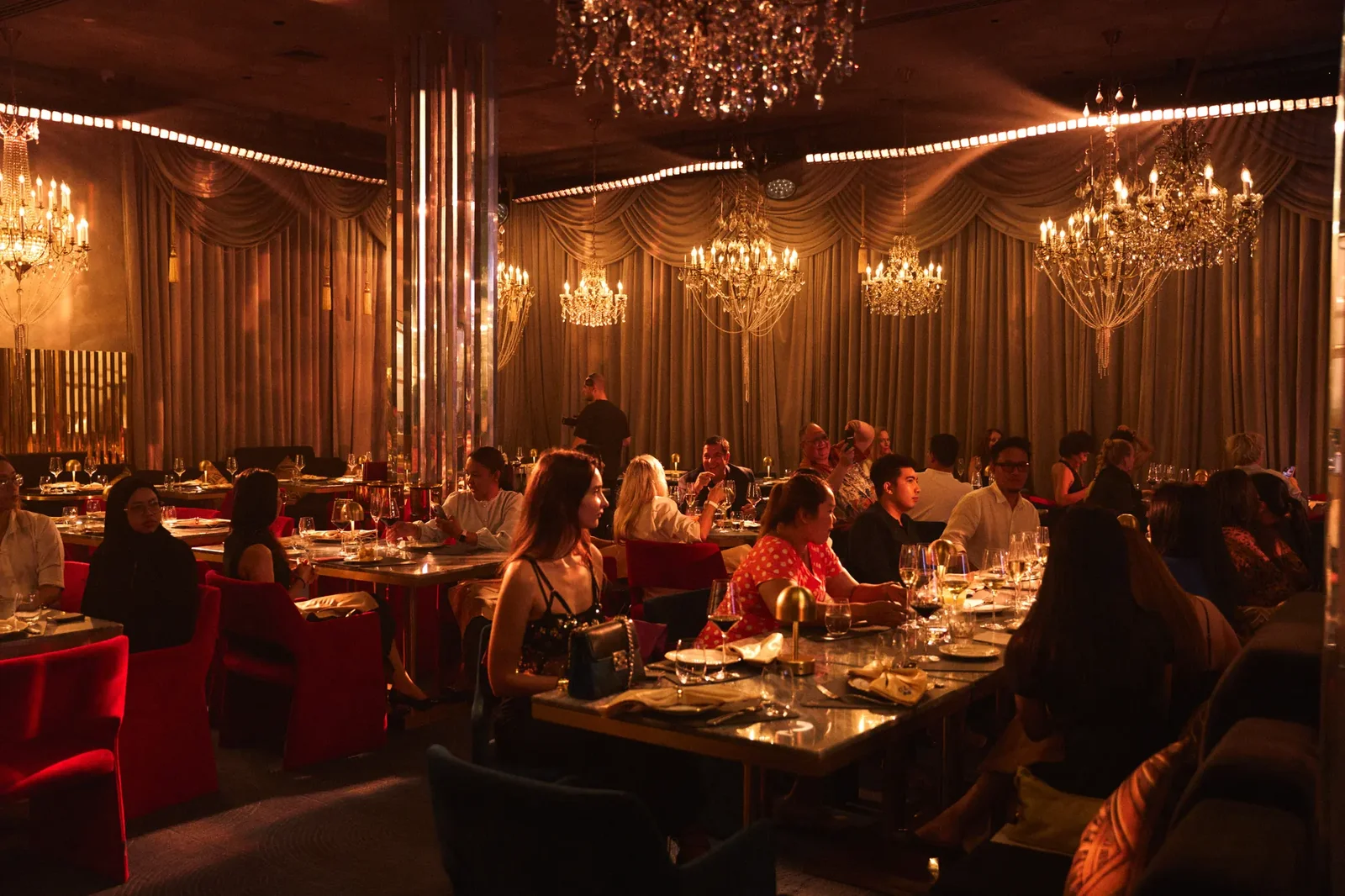 Зрители CLC Dinner & Show сидят за столами под хрустальными люстрами в вечернем зале