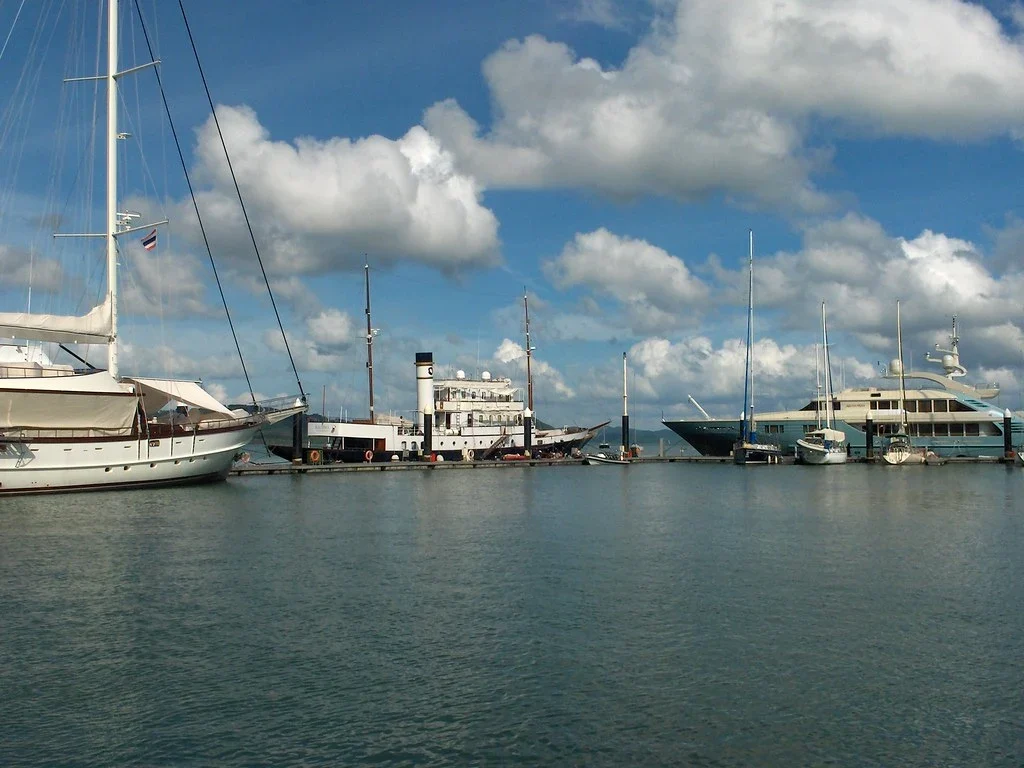 Причал марины Phuket Yacht Haven: яхты и классическое судно с трубой у понтона в солнечный день.