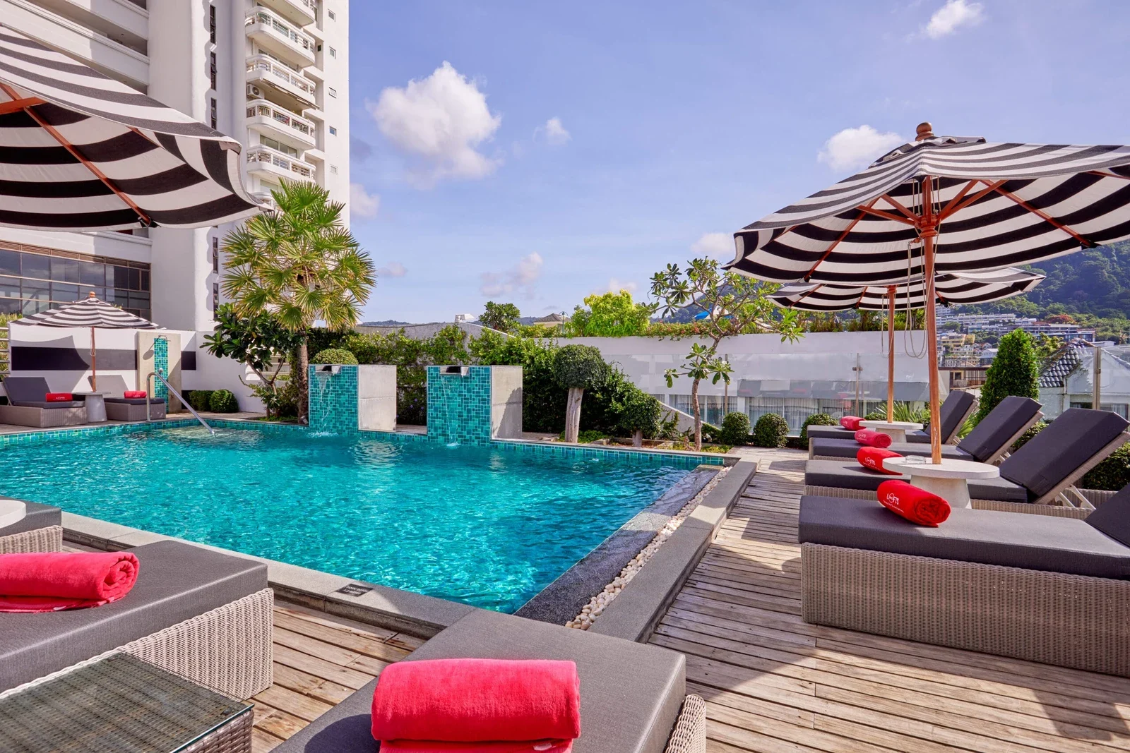 Бассейн BYD Lofts Boutique Hotel & Serviced Apartments с бирюзовой водой, полосатыми зонтами и шезлонгами с красными полотенцами.