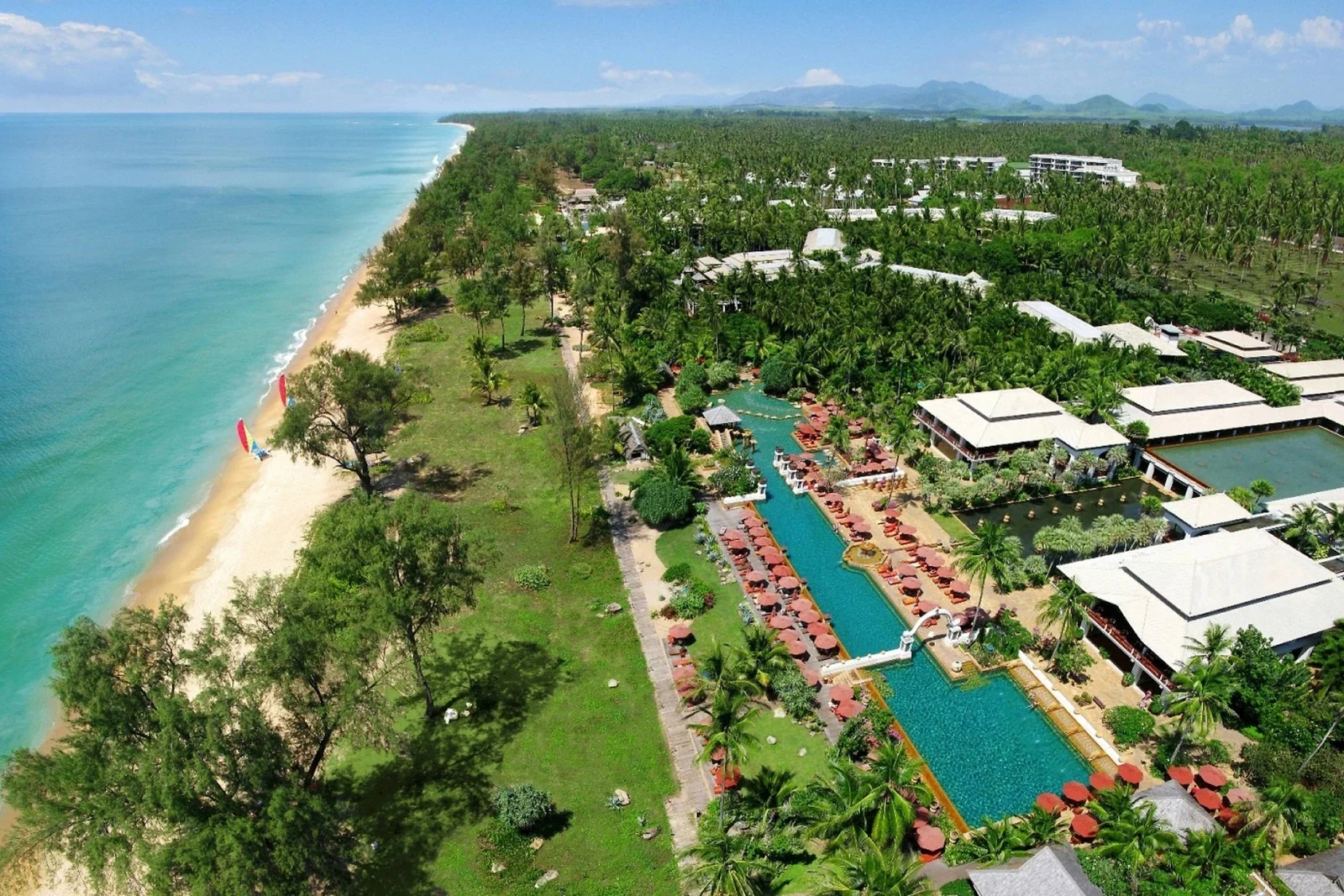 Вид сверху на JW Marriott Phuket Resort & Spa: длинный бассейн, зонты, корпуса среди пальм и пляж с бирюзовым морем