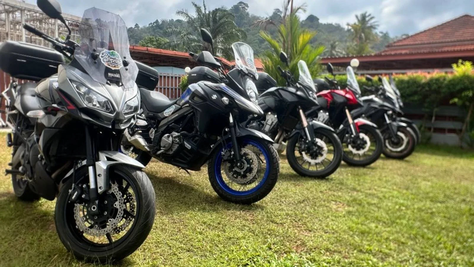Phuket Garage — территория офиса. Ряд туристических мотоциклов перед зданием с красной крышей; официальный кадр Our office.