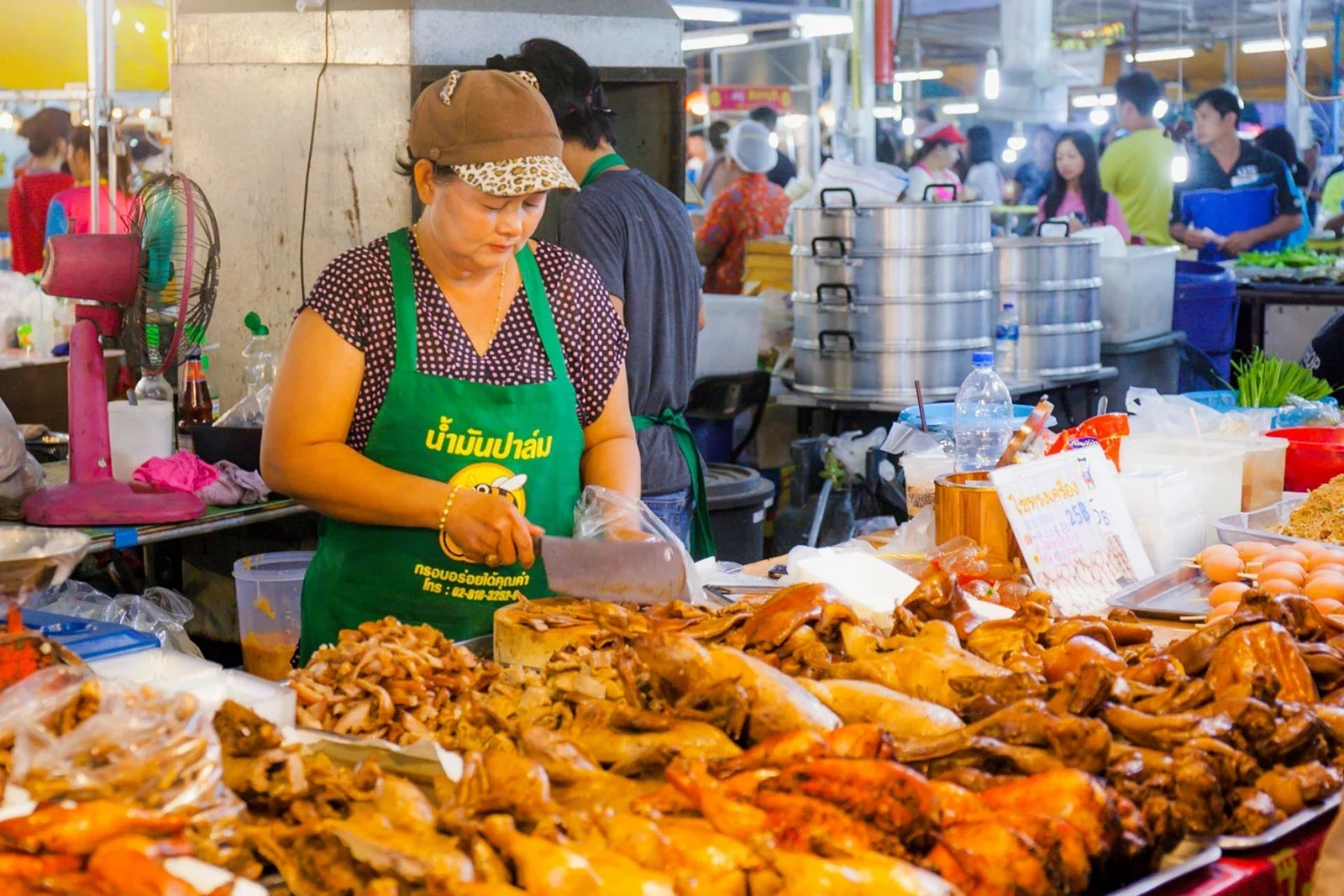 Продавщица нарезает тушёное мясо и птицу у прилавка ночного рынка Нака