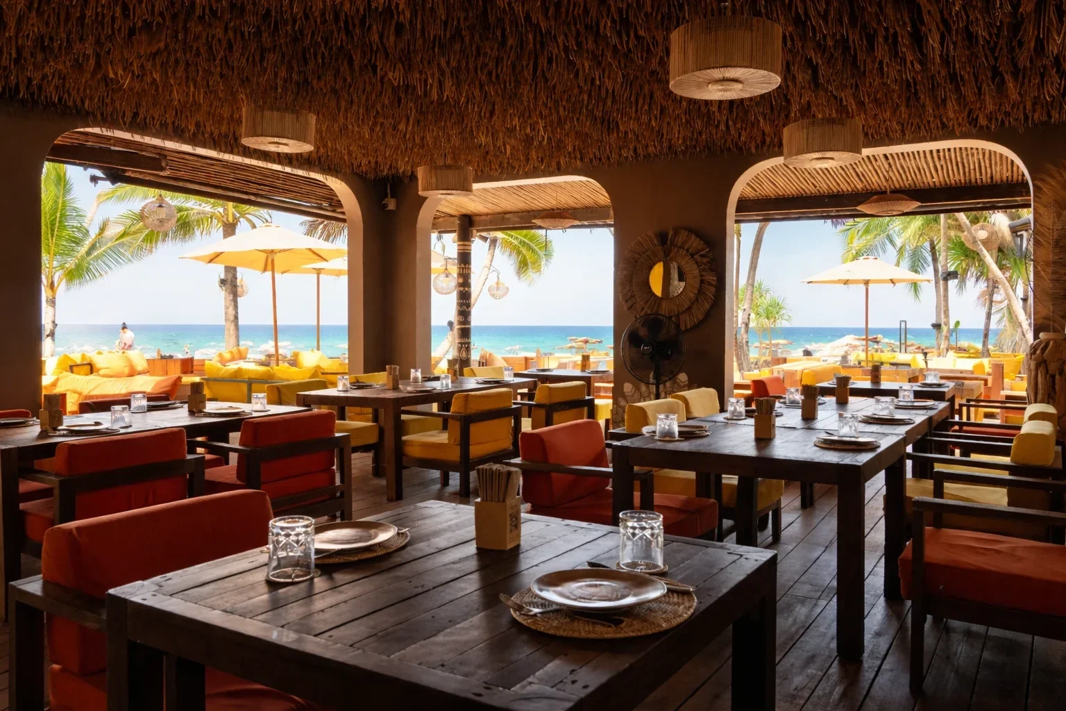 Сервированные деревянные столы и цветные кресла в крытом зале Tann Beach Club