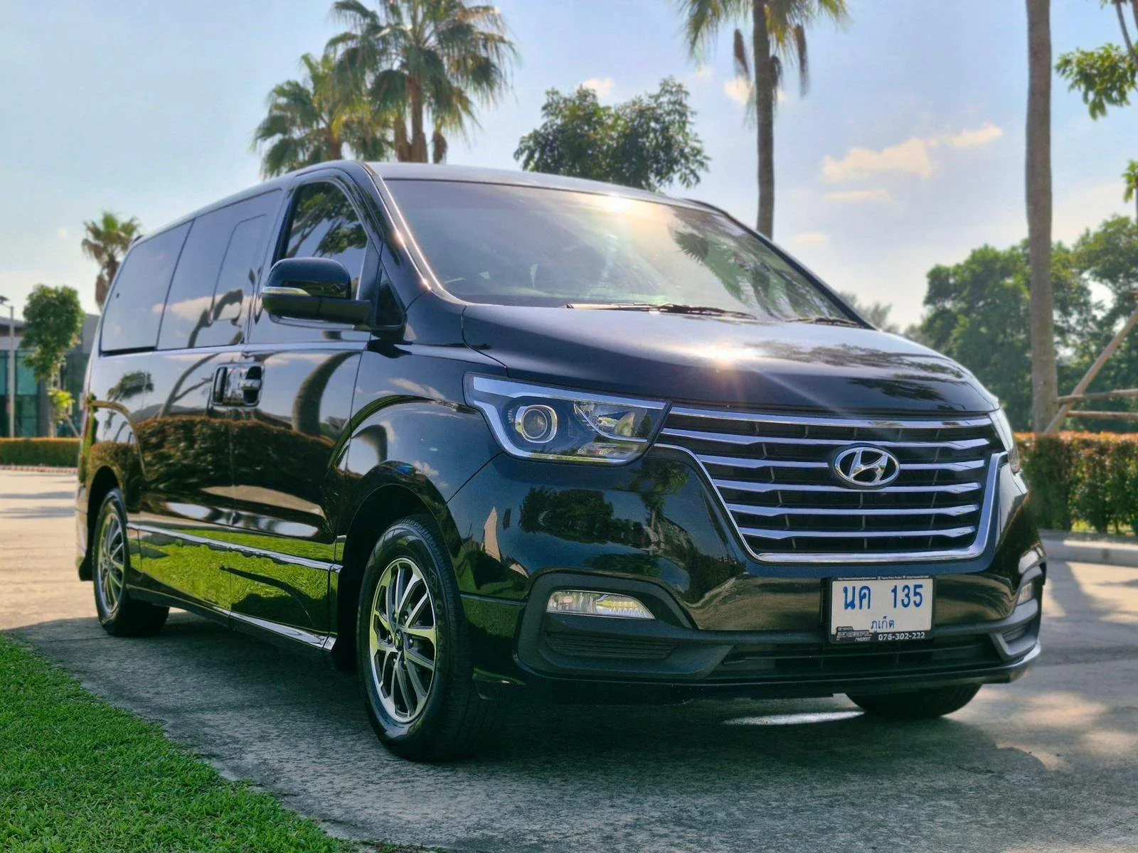 Чёрный минивэн Hyundai H-1 с тайскими номерами, вид спереди на парковке среди пальм