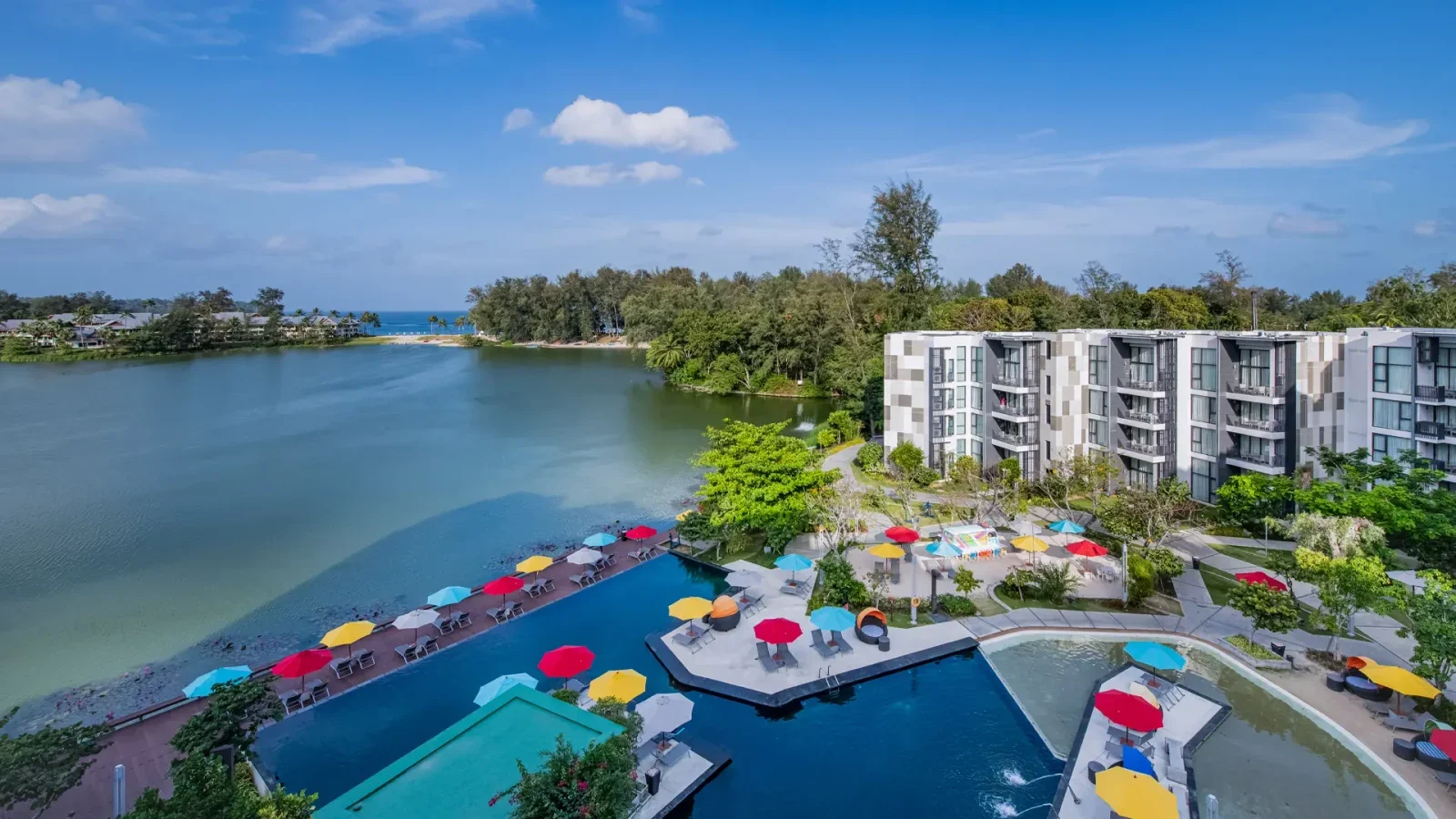 Корпус Cassia Phuket у лагуны: апартаменты, прогулочная набережная, бассейн и яркие зонты.