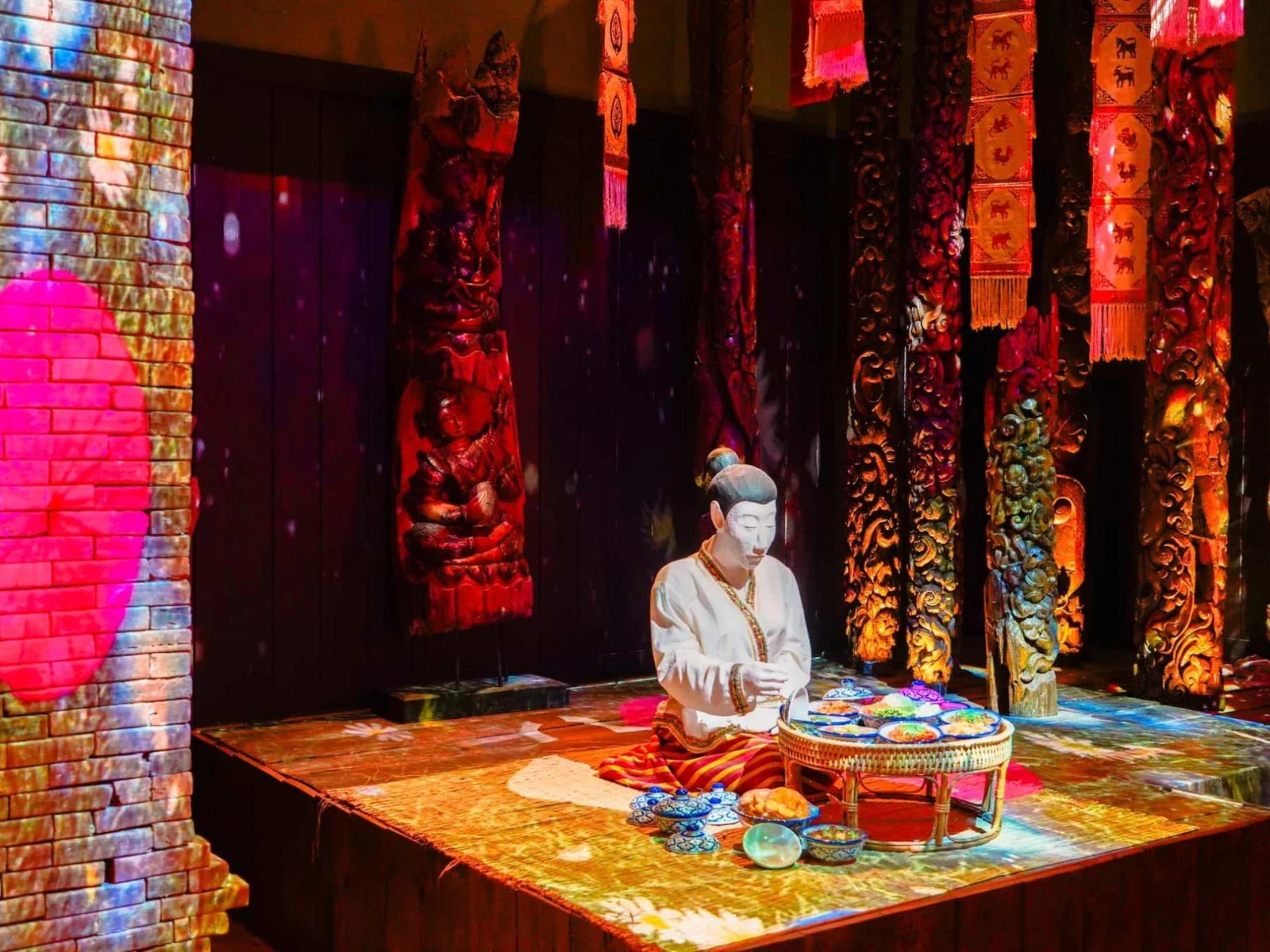 Фигура сидящего мужчины с подносами у резных колонн в Fantastic Phuket Museum