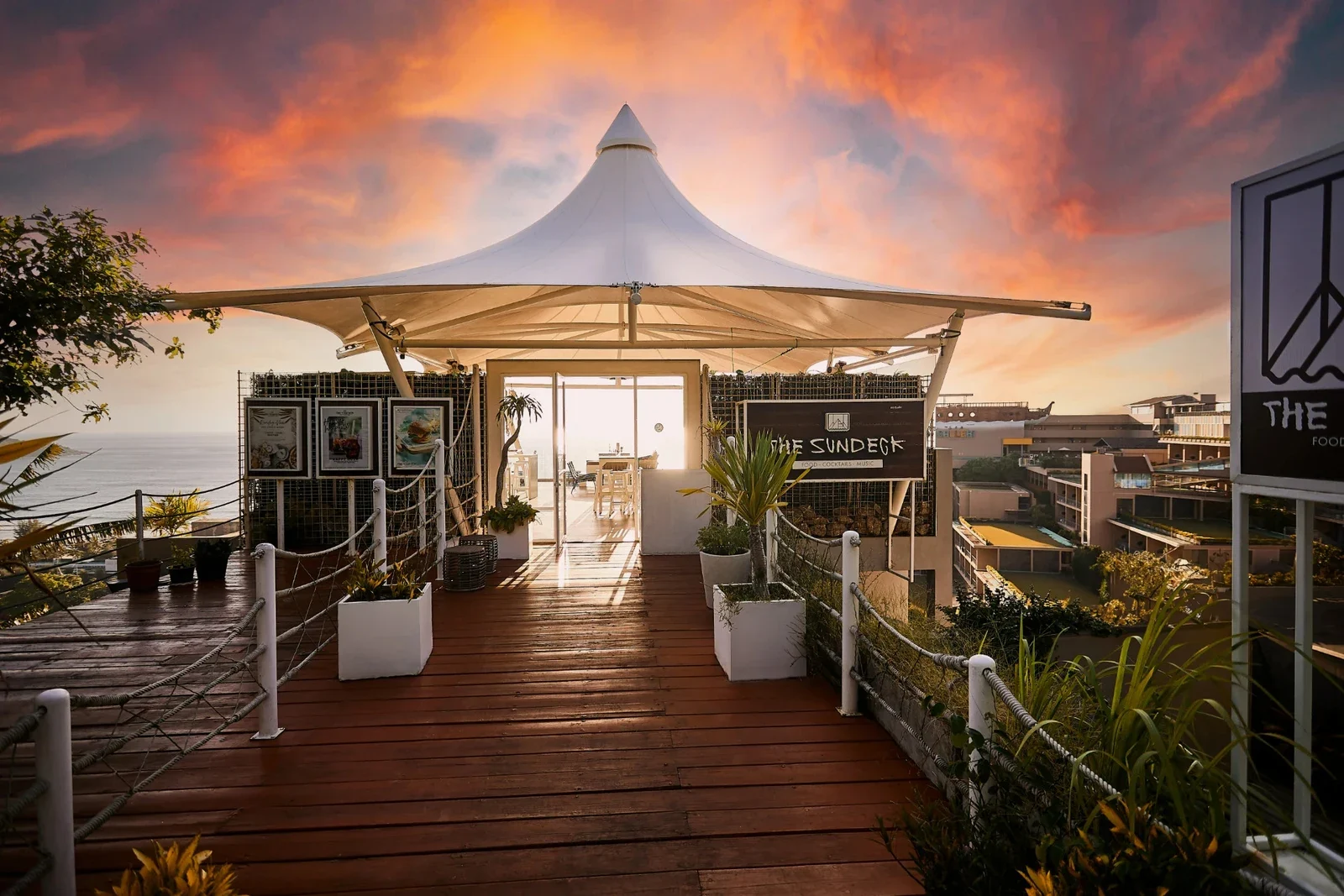 Деревянная палуба и белый шатёр с вывеской The Sundeck над морем на закате