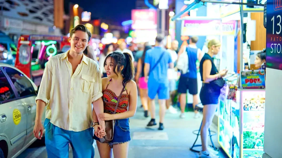 Посетители проходят вдоль открытых торговых прилавков Beyond Night Market у изогнутого фасада отеля