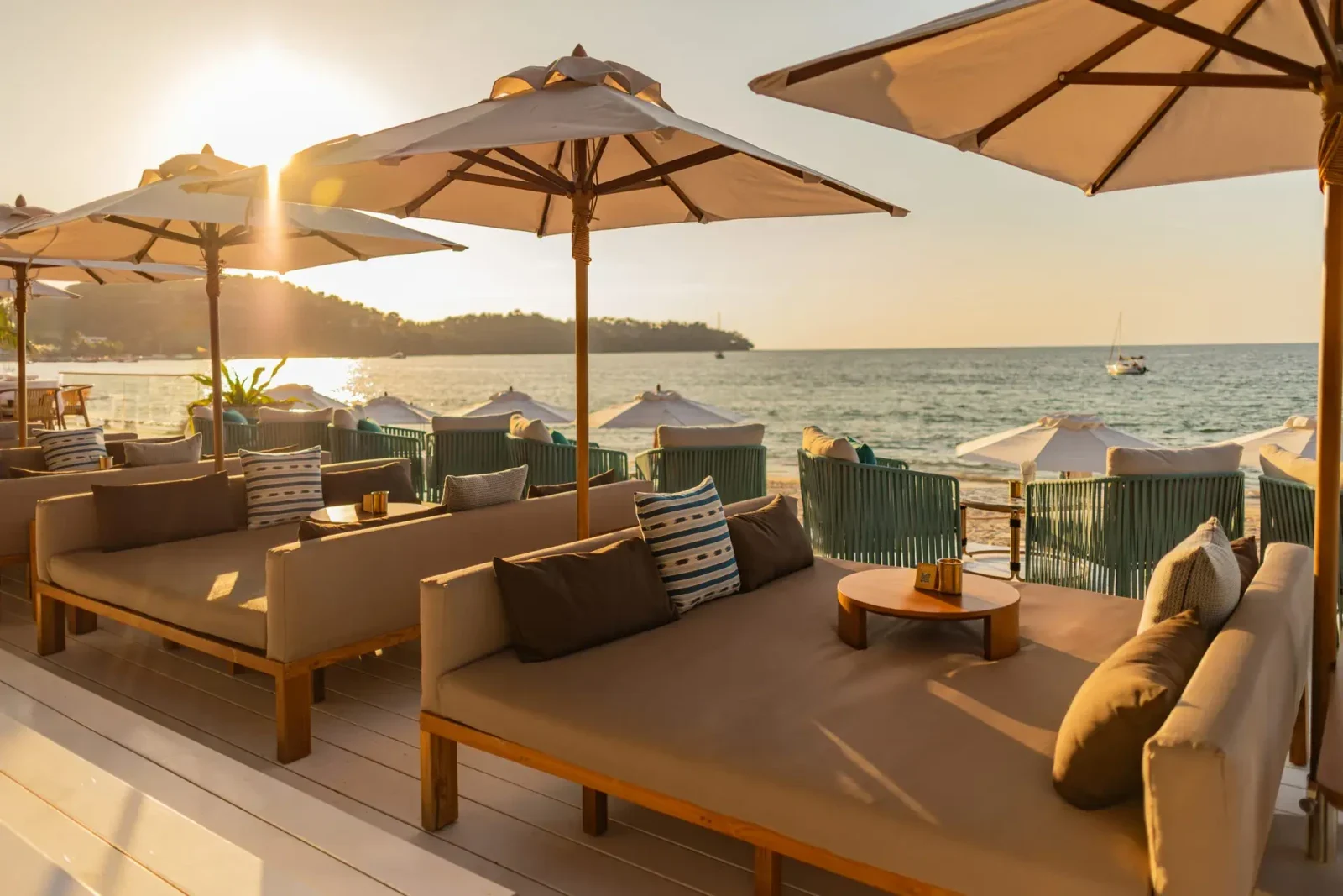 Закат над бухтой Банг Тао: диваны под зонтами на белом деке Catch Beach Club, вдали лодка и мыс