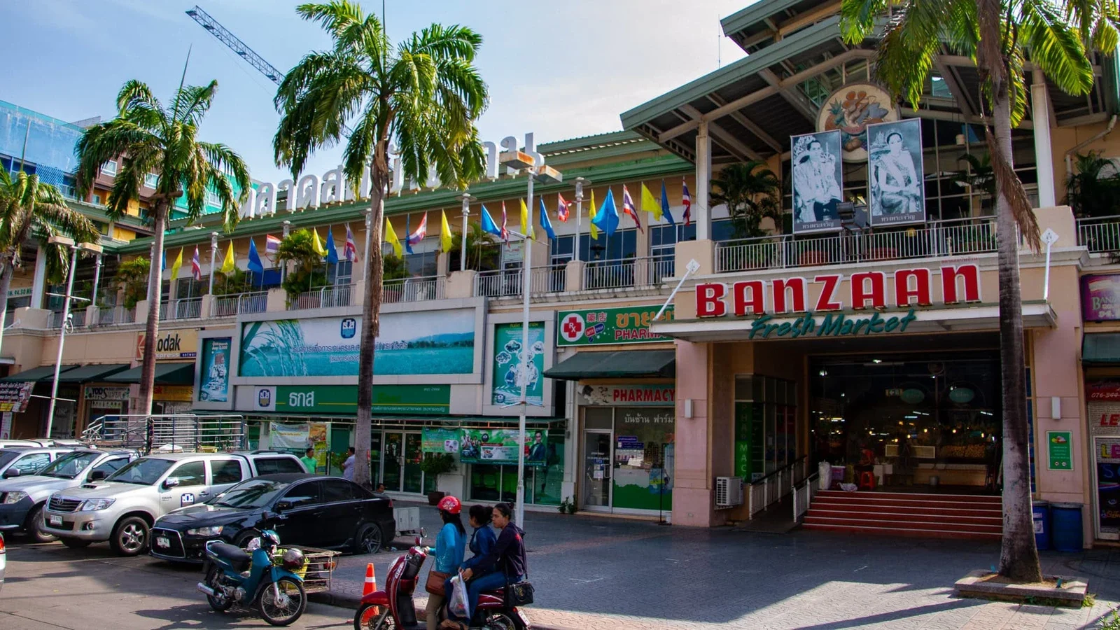 Вход на рынок Banzaan Fresh Market в Патонге: вывеска, флаги, пальмы, припаркованные машины и байки