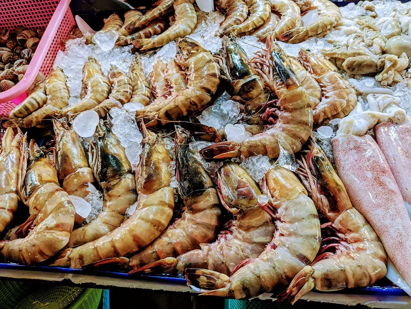 Крупные креветки и кальмары лежат на колотом льду в витрине морепродуктов Bangla Night Market