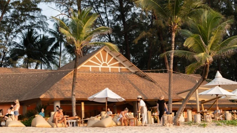 Здание Casuarina Beach Club с зоной отдыха на песке и белыми зонтиками