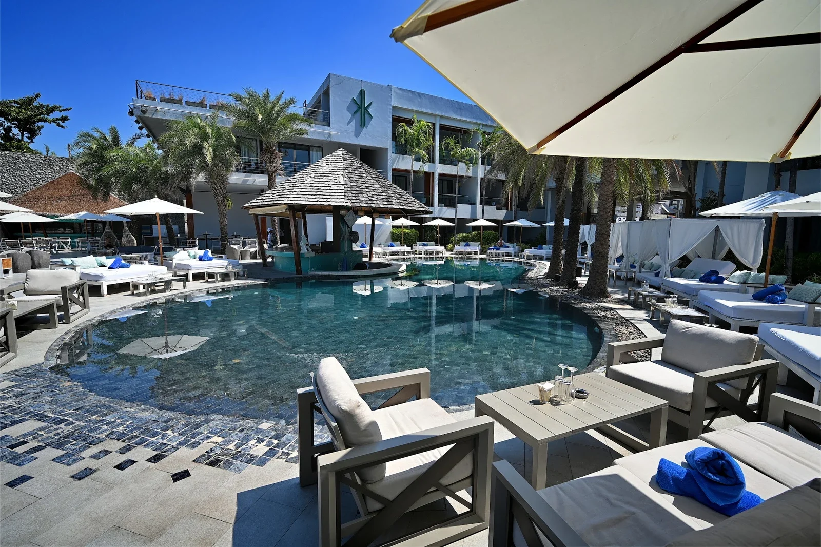 Бассейн и бар под шатровой крышей на KUDO Beach Club, шезлонги и лежаки днём