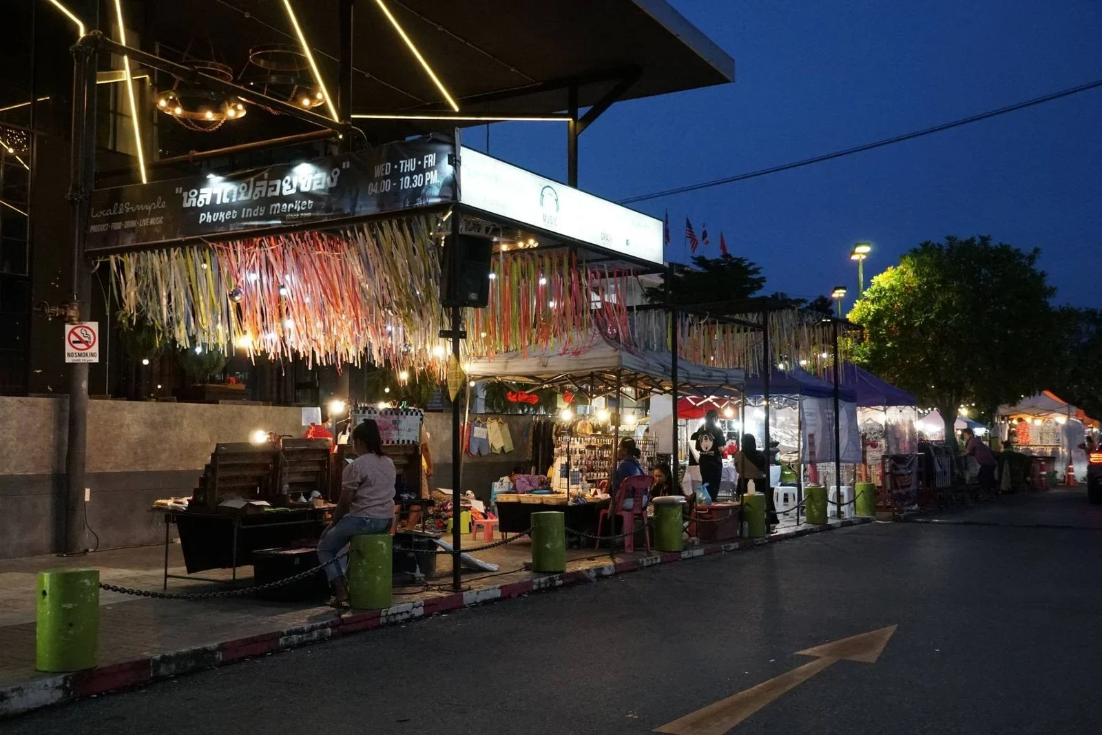 Подсвеченная вывеска Phuket Indy Market и разноцветные ленты над палатками у вечернего входа на рынок.