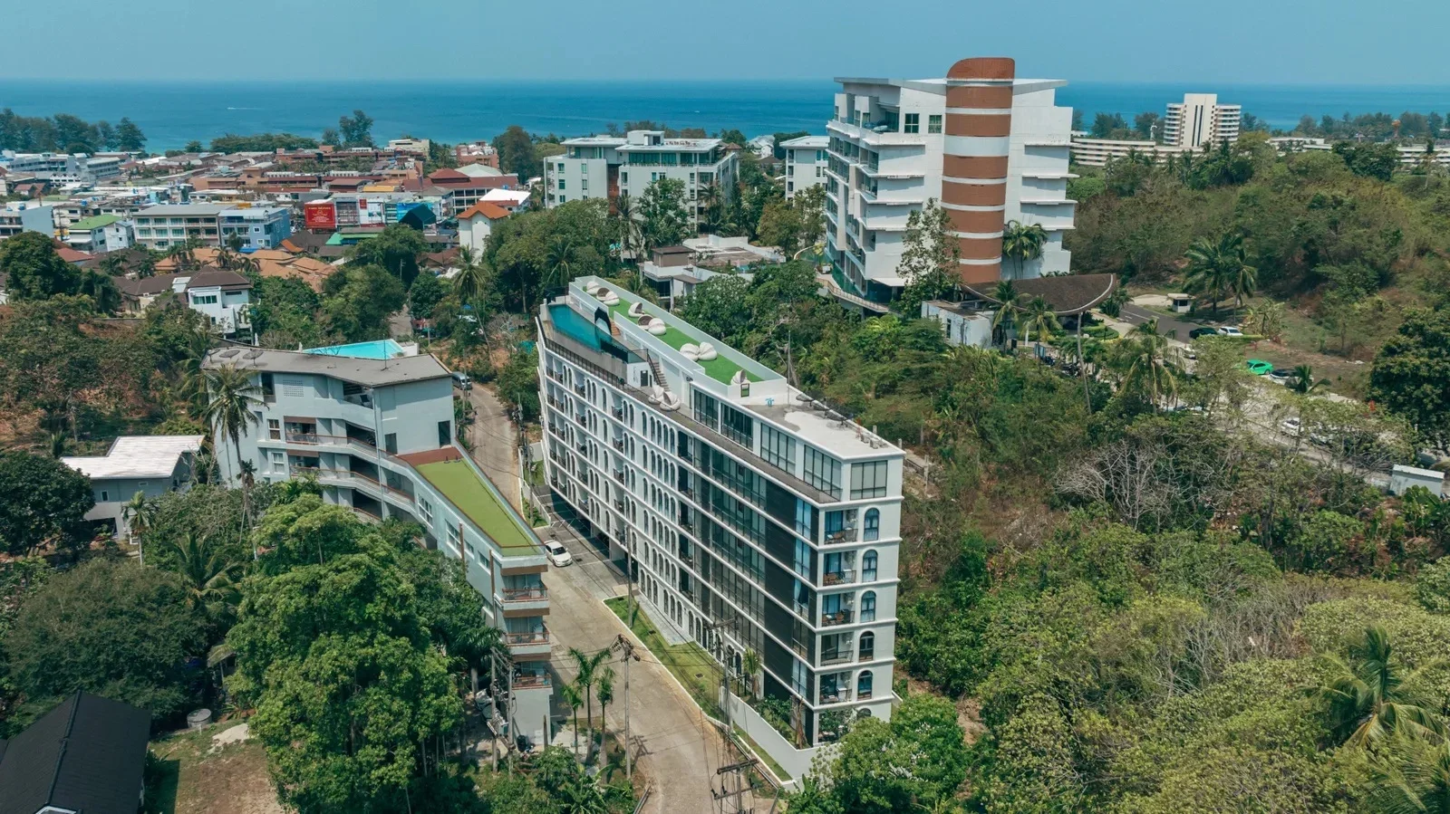 Аэрофото: вытянутый корпус Palmetto Park на склоне среди зелени, вдали залив и Карон