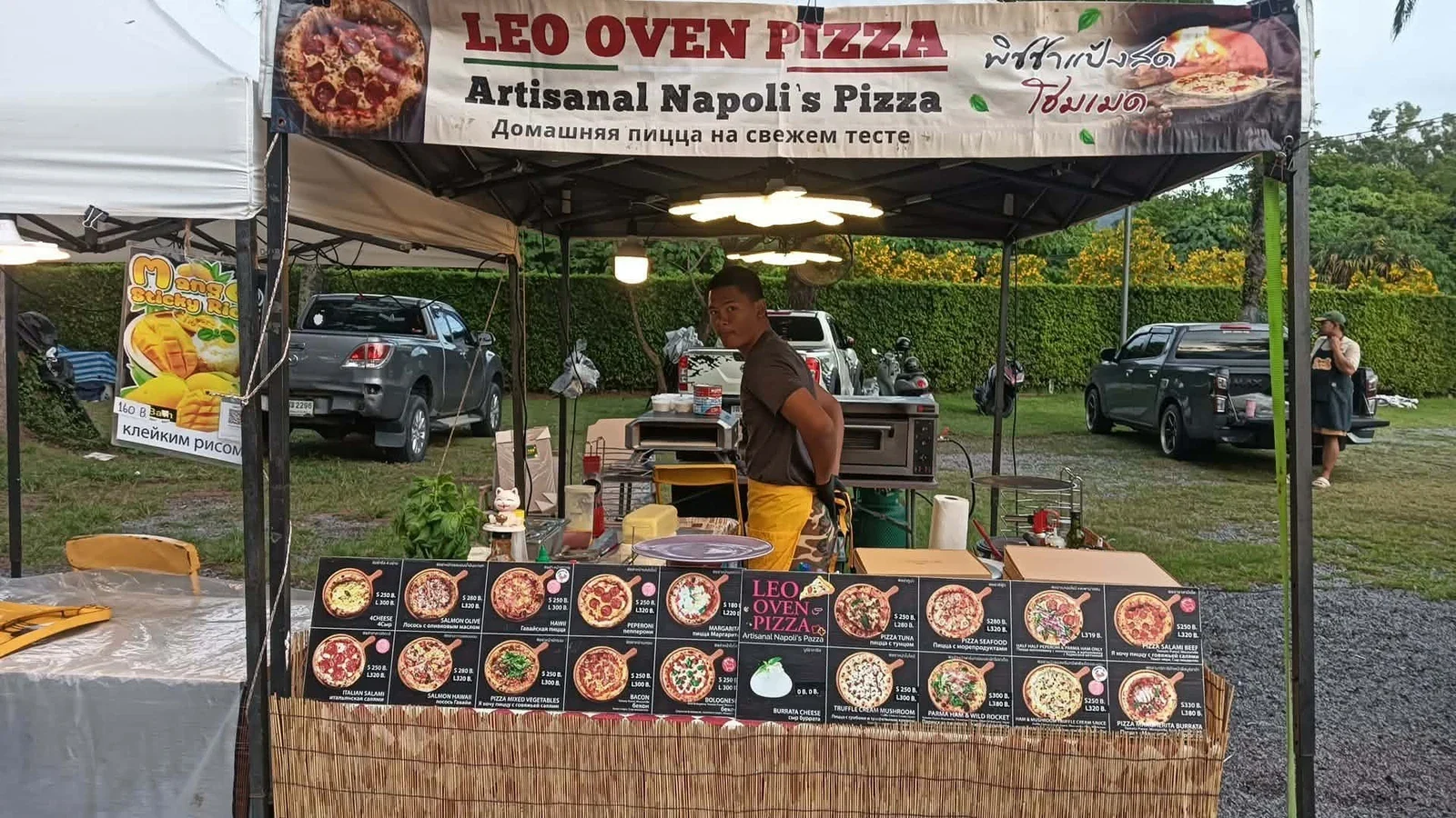 Продавец у палатки Leo Oven Pizza на Laguna Lifestyle Night Market; под навесом стоят печи для пиццы.