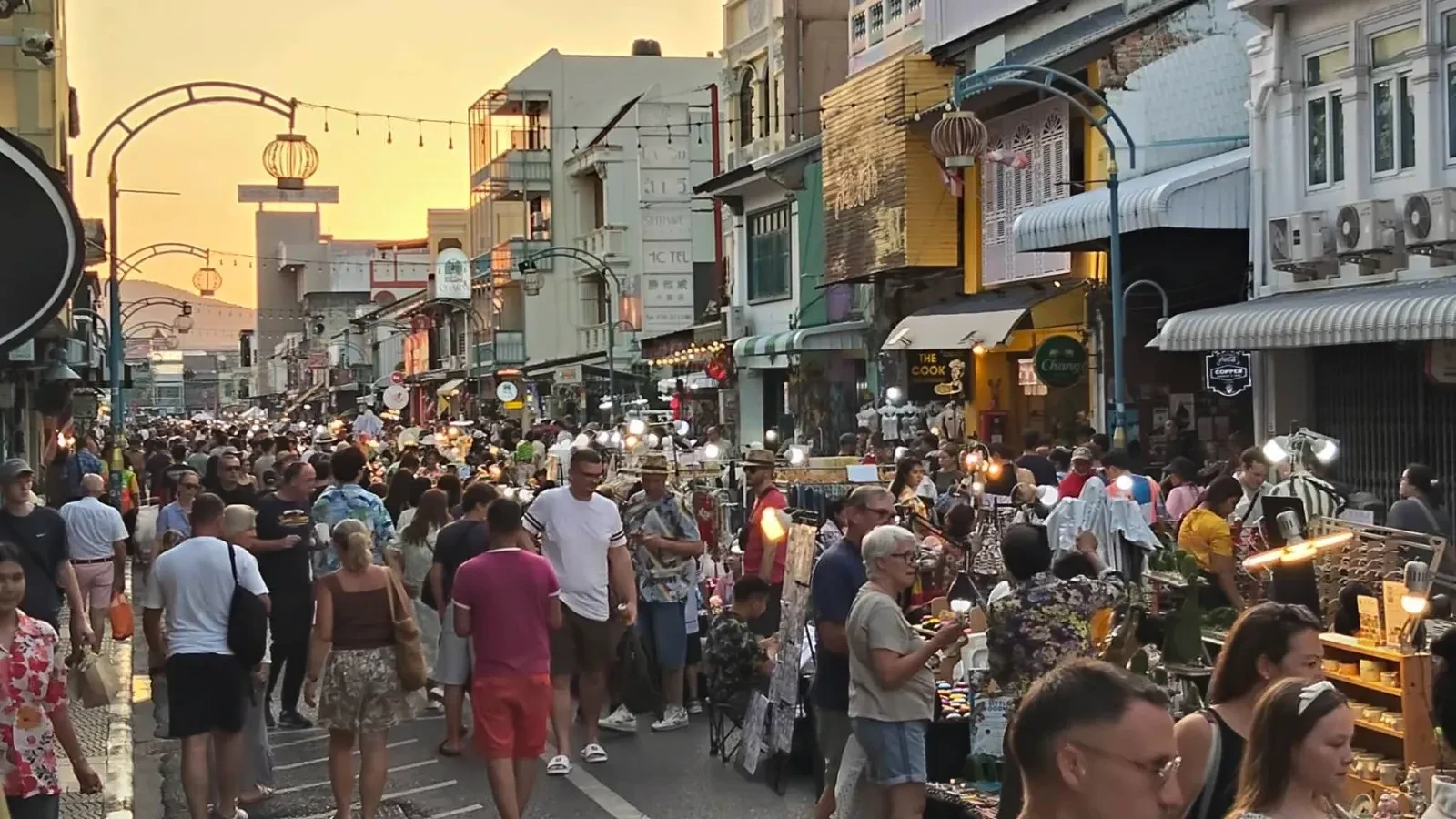 Толпа посетителей проходит между торговыми рядами Chartered Walking Street в свете заката