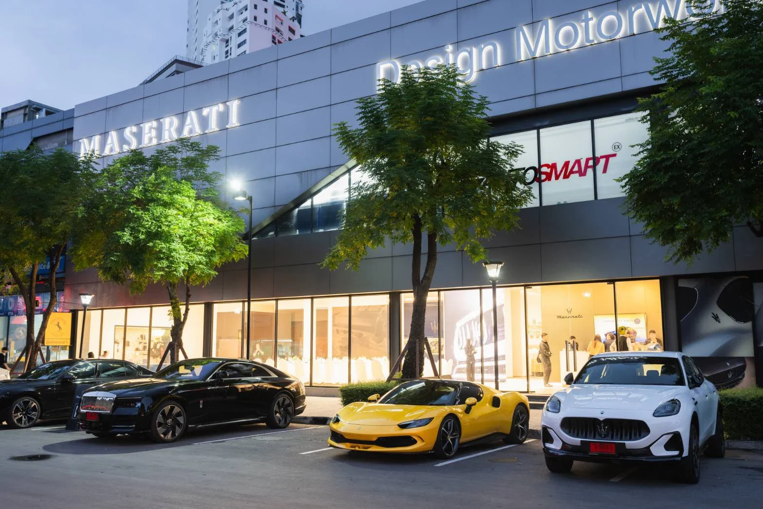 Вечером у премиум-шоурума припаркованы жёлтый Ferrari 296, белый Maserati Grecale и чёрные представительские автомобили проката