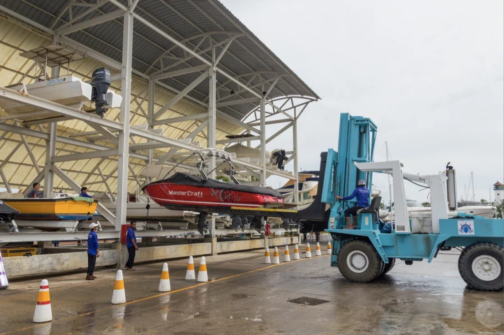 Рабочие Phuket Boat Lagoon перемещают катер MasterCraft вилочным погрузчиком у стеллажей крытого эллинга.