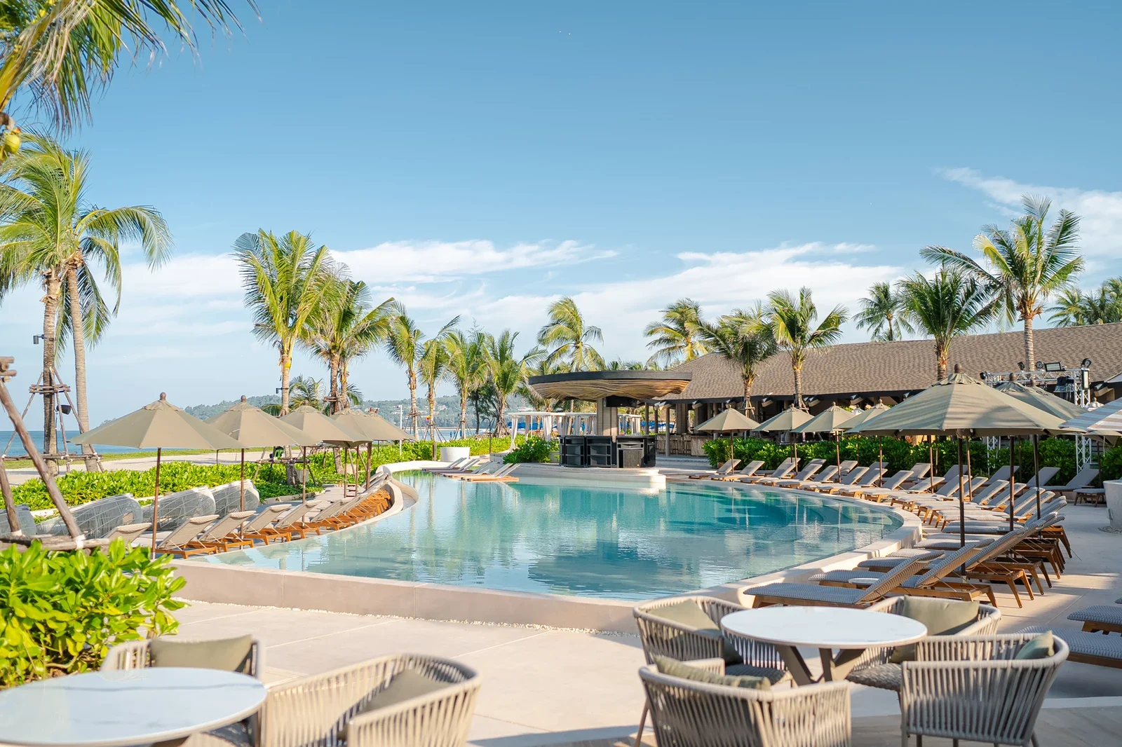 Бассейн RAVA Beach Club с шезлонгами и зонтами, пальмы, бар у воды и море на горизонте