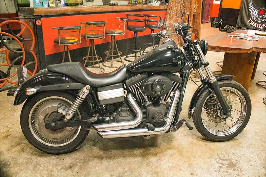 Чёрный Harley-Davidson со спицованным передним колесом стоит в профиль у стойки Southern Big Bike.