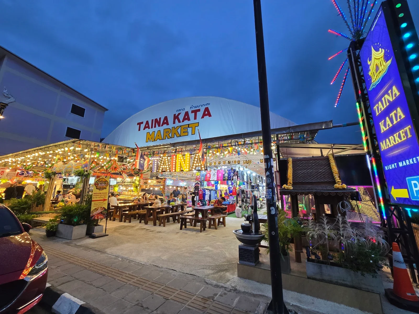 Вход на рынок Taina Kata Market (Kata Night Market) вечером: белый купол с вывеской и ряды столиков