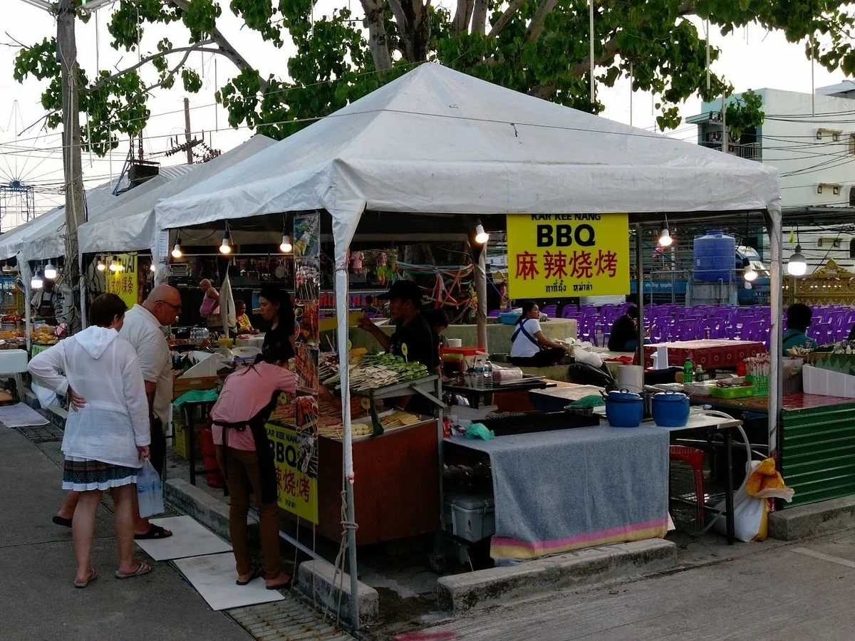 Ряды палаток под белыми тентами на улице у храма, жарят BBQ, покупатели и гирлянды