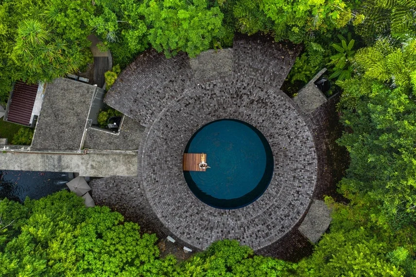 Круглая крыша и водный двор Quan Spa среди деревьев, вид сверху