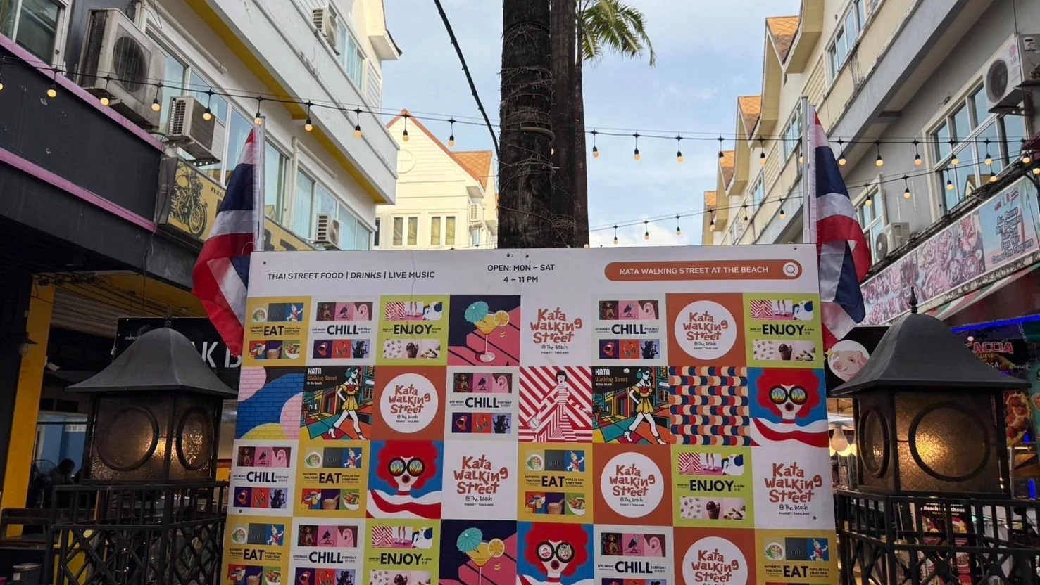 Указатель Kata Walking Street at The Beach между торговыми зданиями и гирляндами у входа