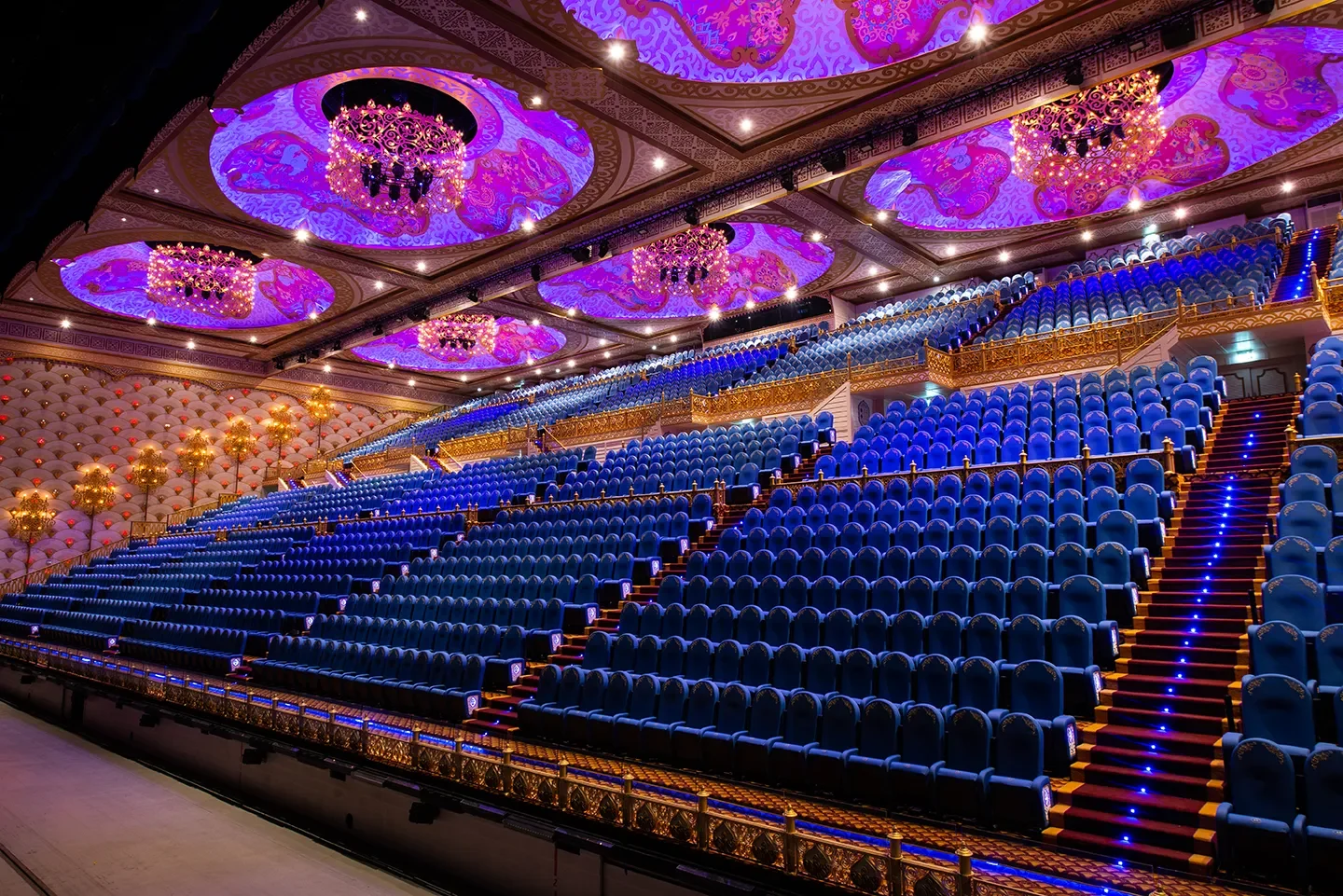 Ряды синих кресел под освещённым декоративным потолком крытого зала River Palace в Carnival Magic