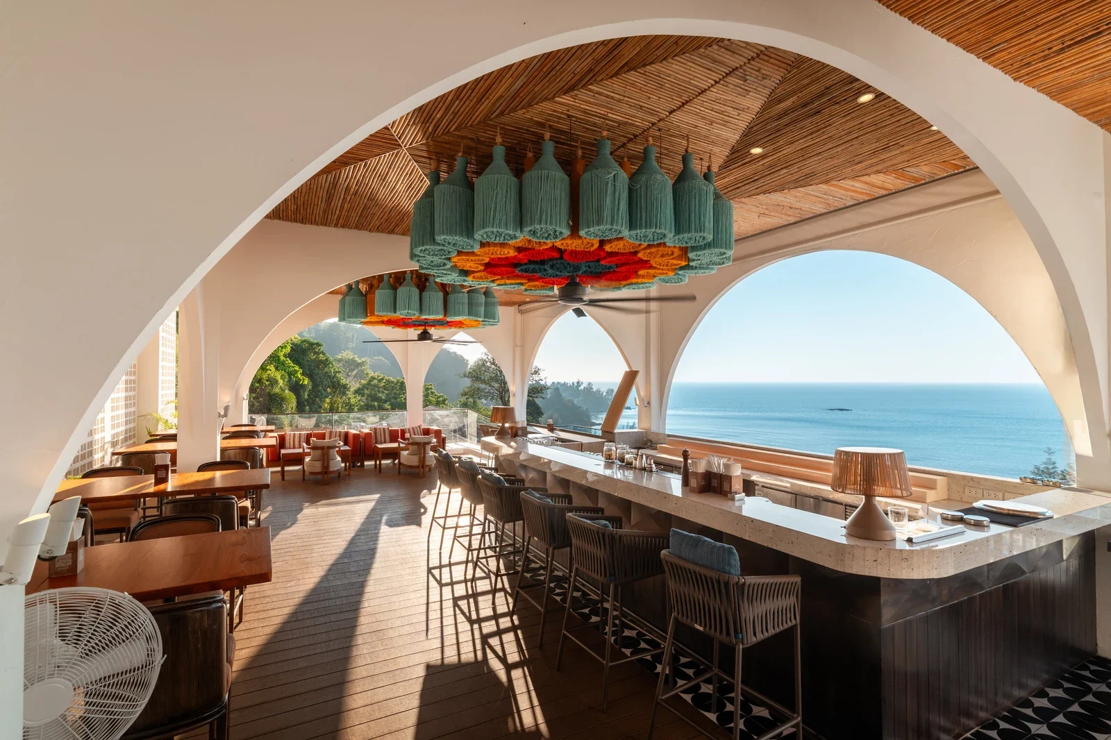 Бар Casa Boho под белыми арками с бамбуковым потолком и видом на море, барные стулья вдоль мраморной стойки