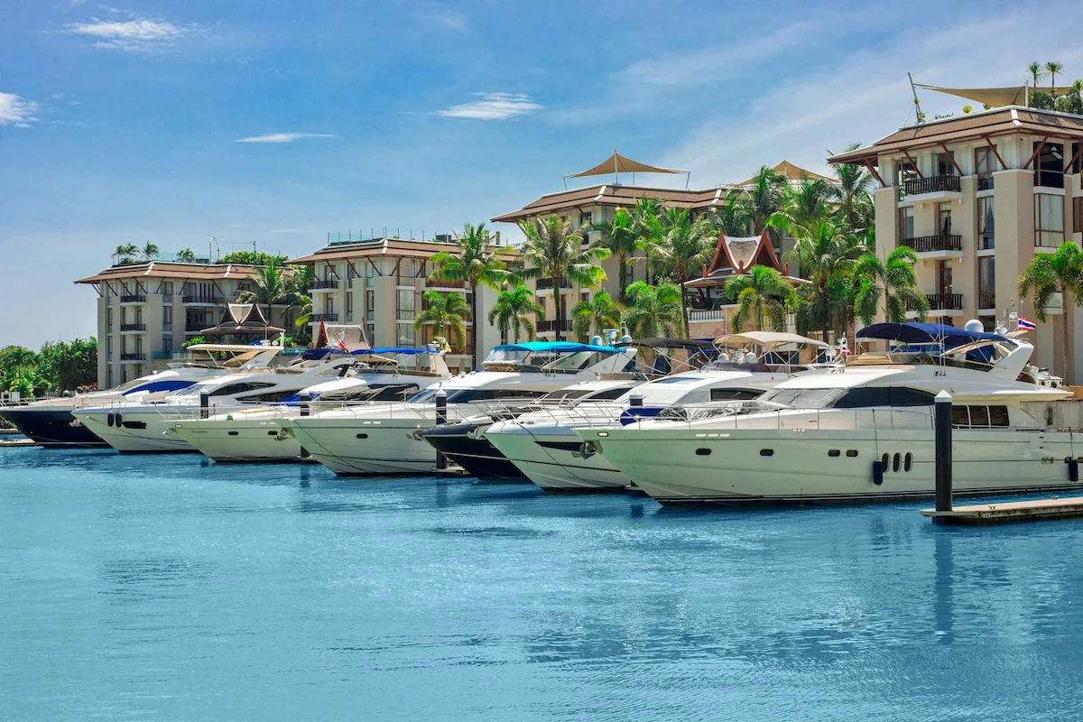 Яхты у понтона Royal Phuket Marina днём: бирюзовая вода, пальмы и жилые корпуса марина-виллидж.