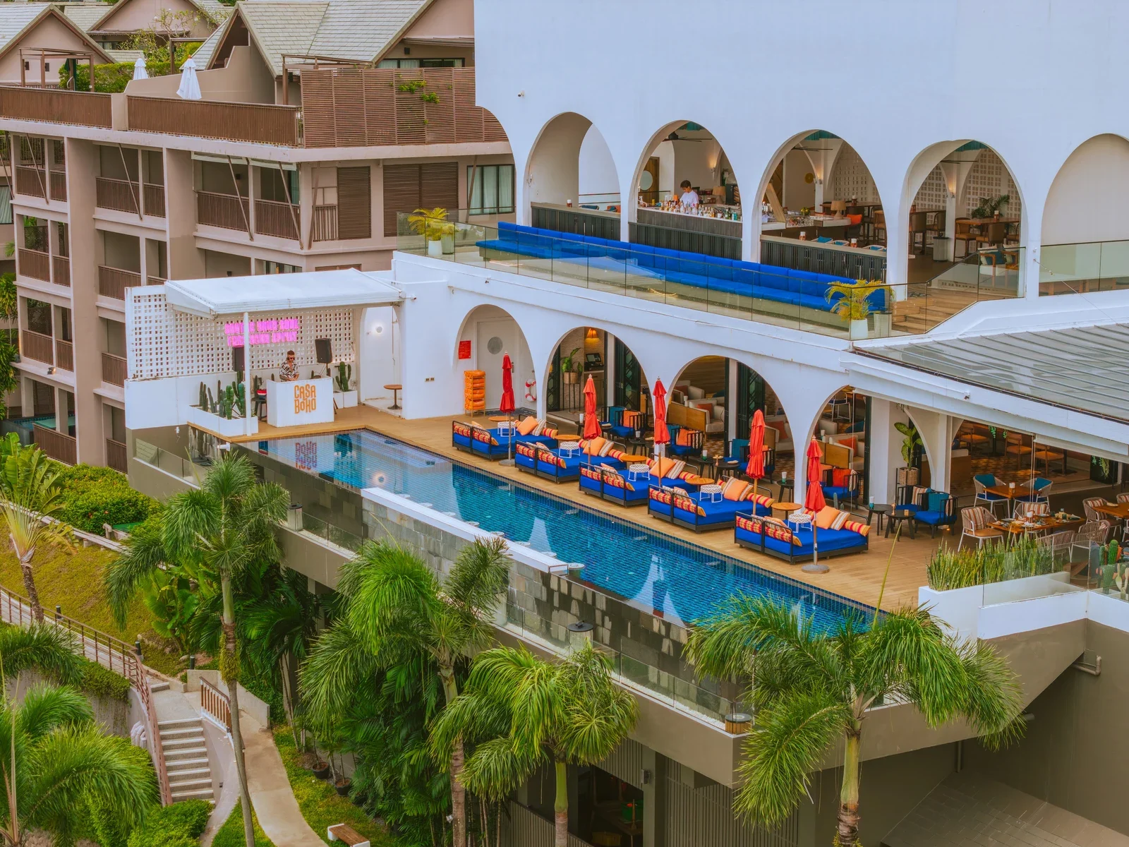 Casa Boho Phuket сверху: бассейн с синими шезлонгами, арочные галереи ресторана и DJ-площадка у воды