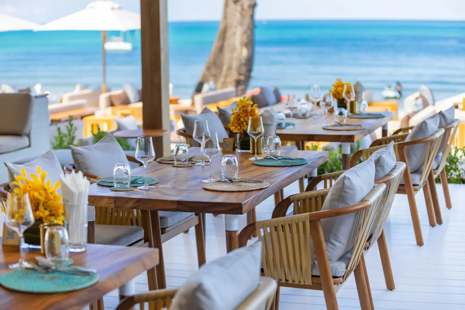 Сервированные столы с плетёными стульями под навесом ресторана Catch Beach Club