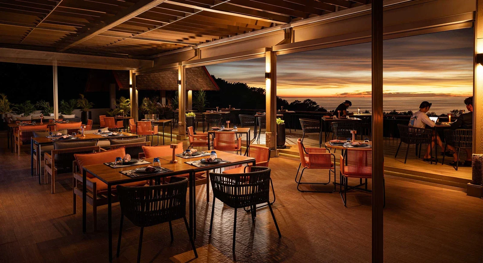Обеденная зона Sizzle Rooftop под деревянной кровлей, за колоннами горит закат