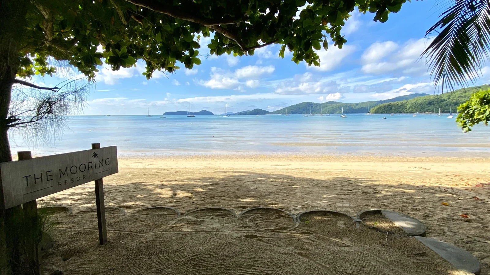 Табличка отеля The Mooring Resort на песке у бухты Ао Йон, яхты и холмы на горизонте