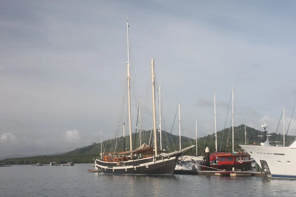 Парусная шхуна и яхты у причала марины Yacht Haven на Пхукете на фоне зелёных холмов