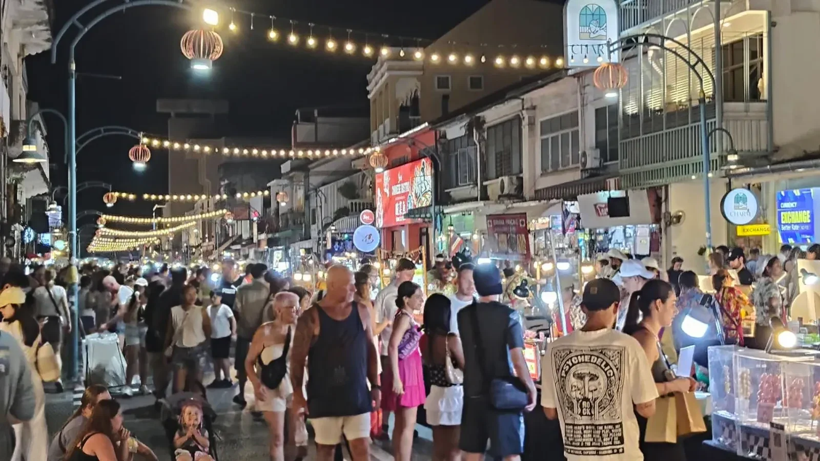 Посетители гуляют между освещёнными палатками Chartered Walking Street под гирляндами над улицей