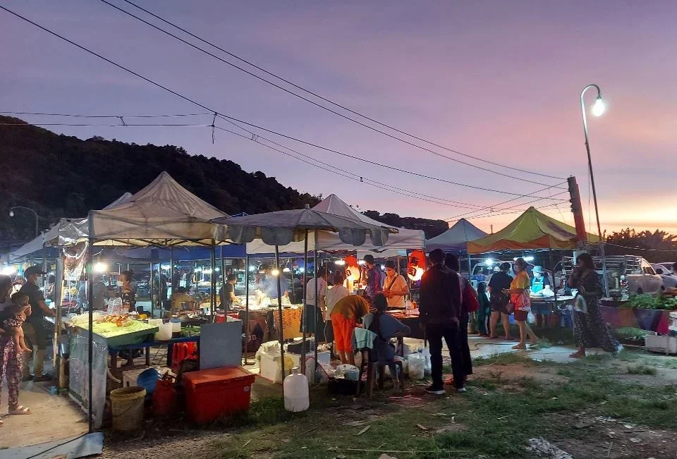 Посетители покупают еду под разноцветными тентами New Kata Night Market на фоне закатного неба