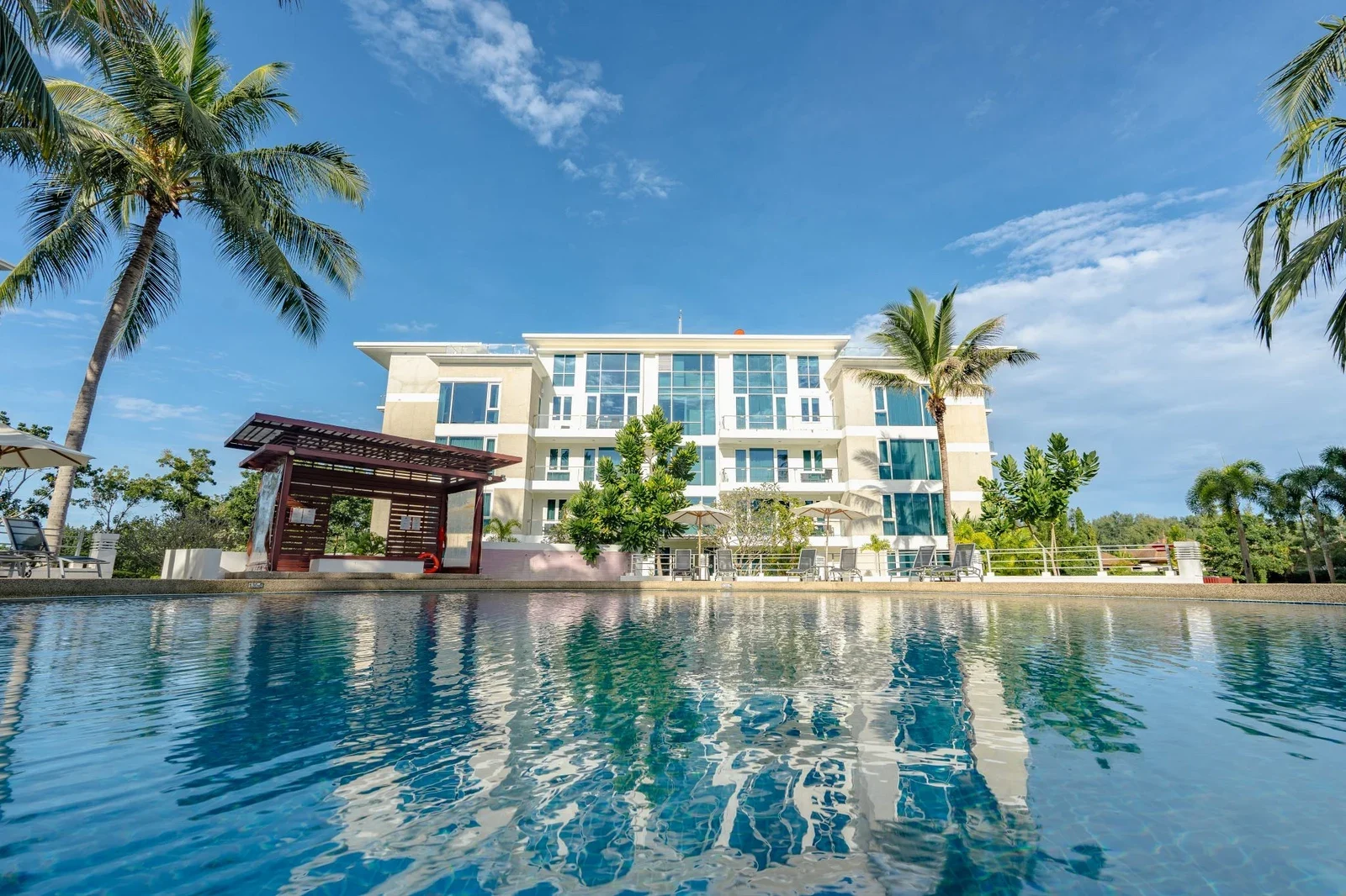 Бассейн Ocean Swimming Pool с видом на белый корпус Splash Beach Resort, беседку и пальмы под синим небом
