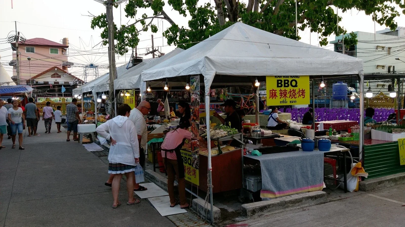 Ряды палаток под белыми тентами на улице у храма, жарят BBQ, покупатели и гирлянды