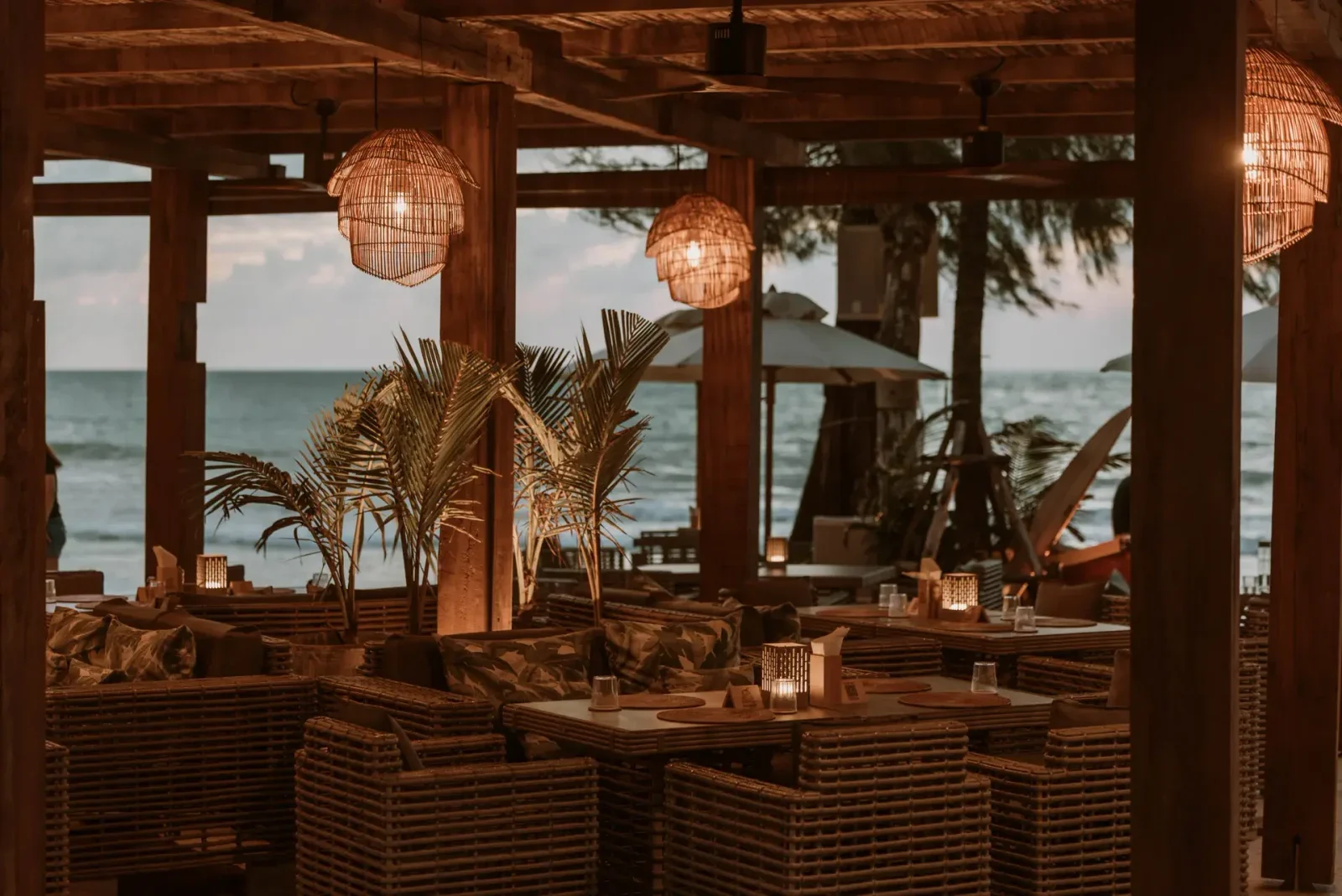 Сервированные столики и плетёные светильники под навесом ресторана The Lazy Coconut