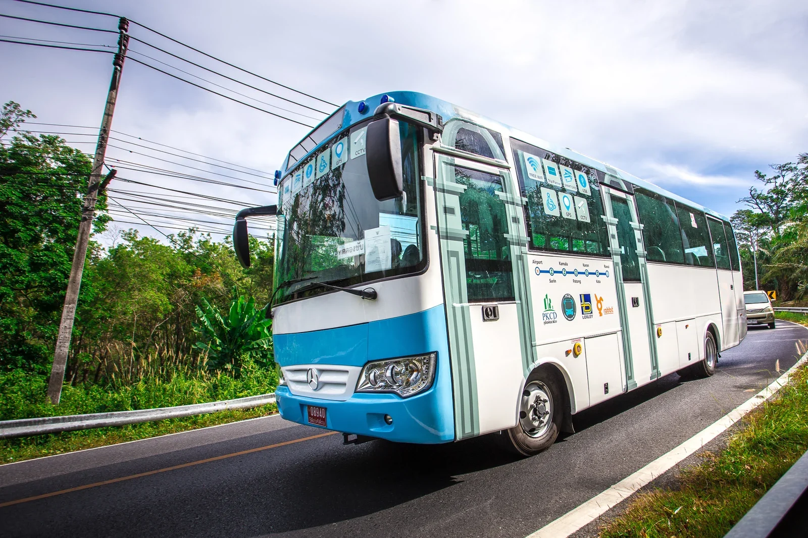 Сине-белый автобус Phuket Smart Bus едет по зелёной дороге Пхукета, на борту маршрут и логотип rabbit.