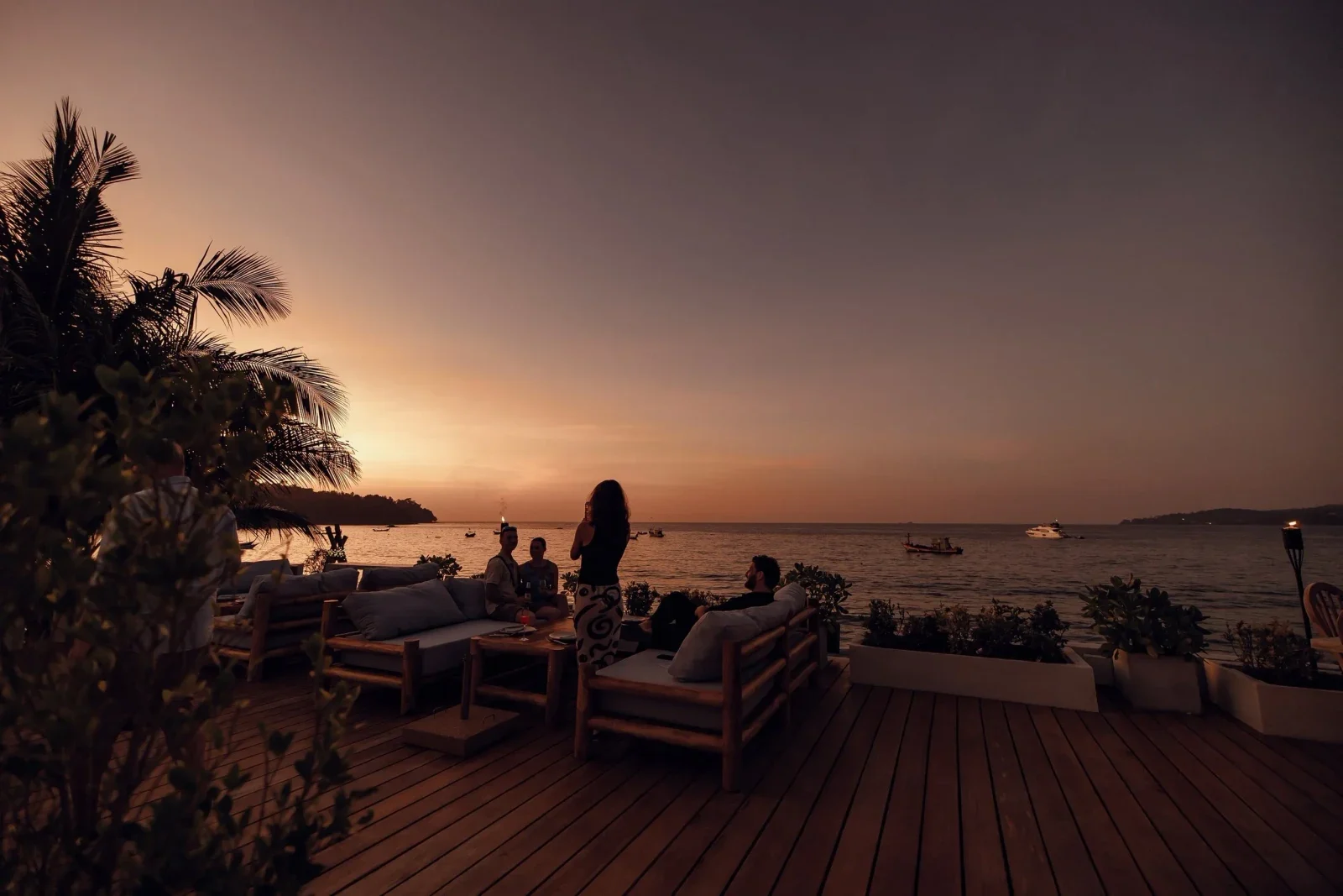 Деревянная палуба GOAT Beach Club с диванами и отдыхающими на фоне закатного моря