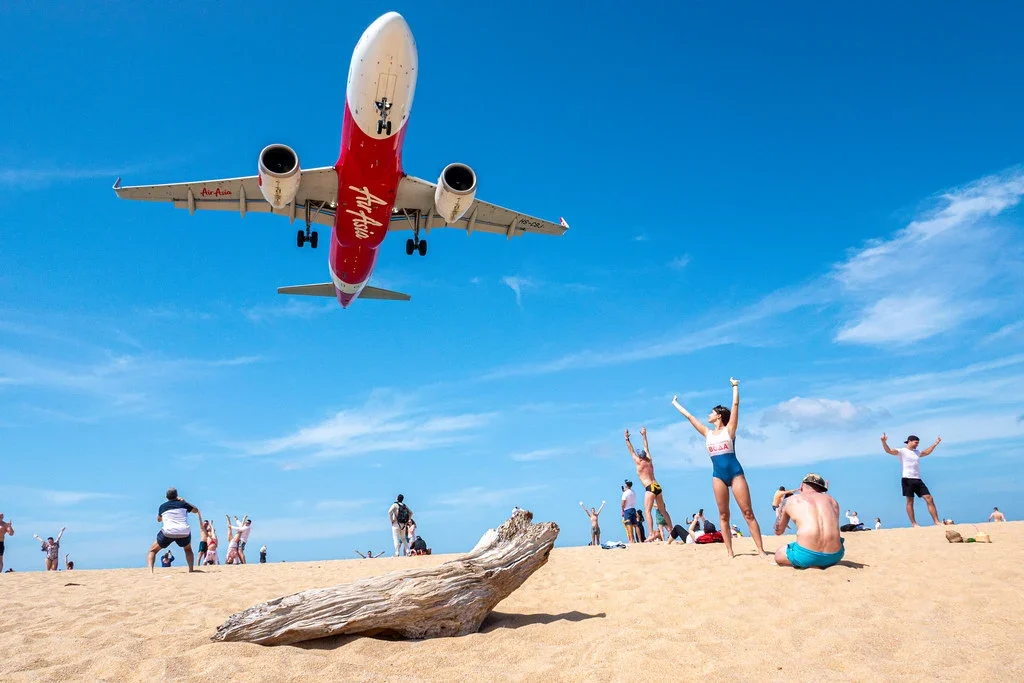 Самолёт AirAsia заходит на посадку низко над пляжем Най Янг, отдыхающие на песке машут и фотографируют его