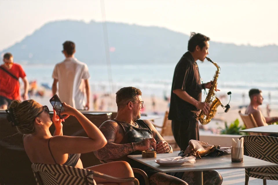 Саксофонист выступает у столиков FUGA Beach Club на берегу Патонга