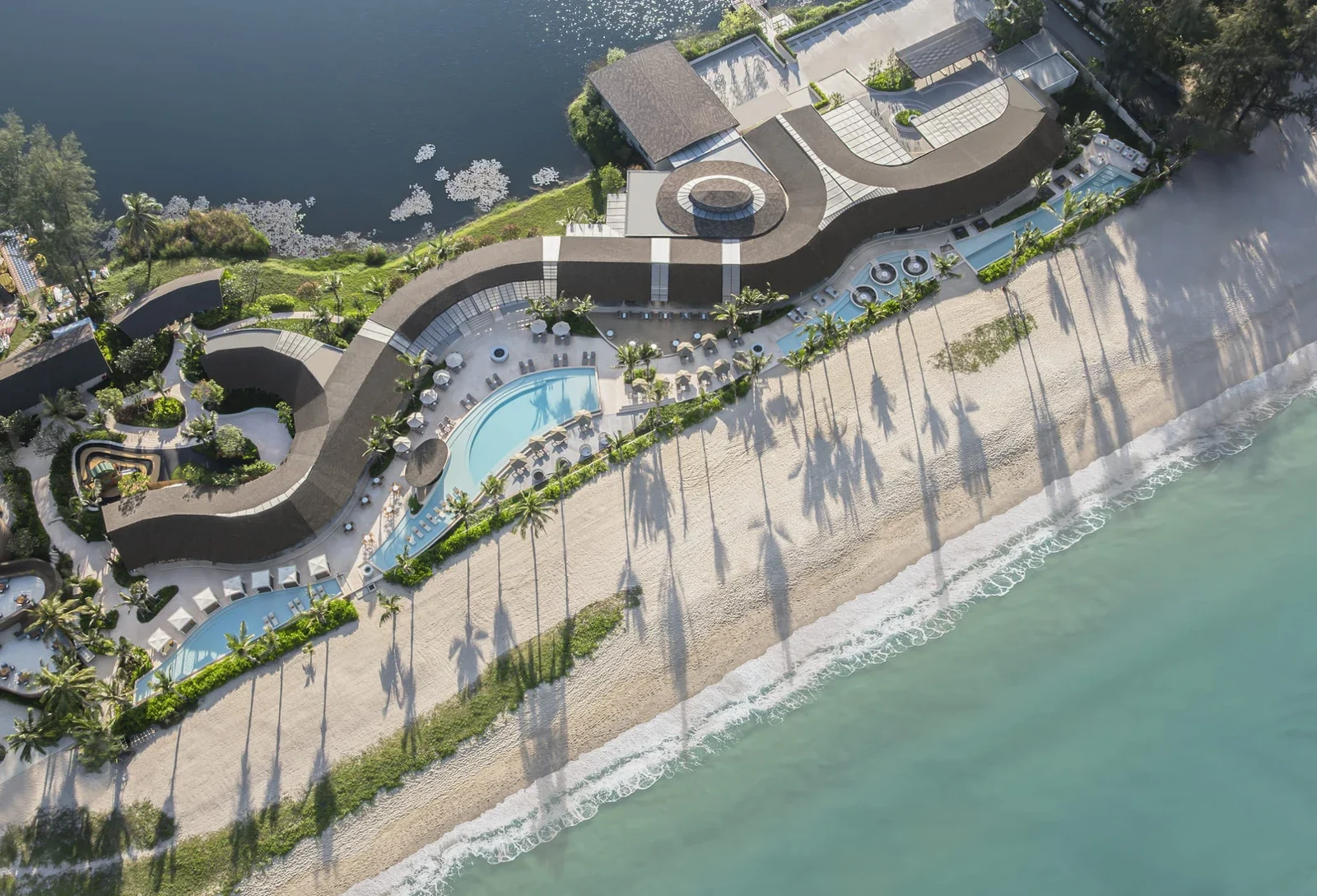RAVA Beach Club с высоты: изогнутая крыша клуба, бассейны вдоль пляжа с белым песком и бирюзовое море