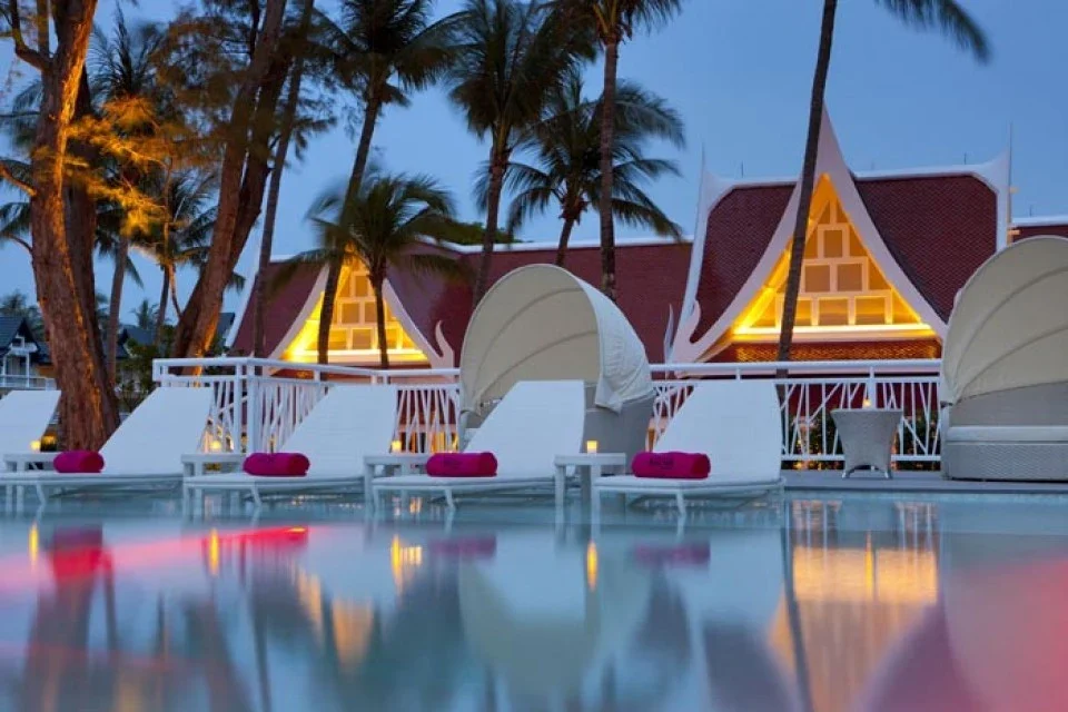 Белые лежаки у бассейна XANA Beach Club возле подсвеченных зданий вечером