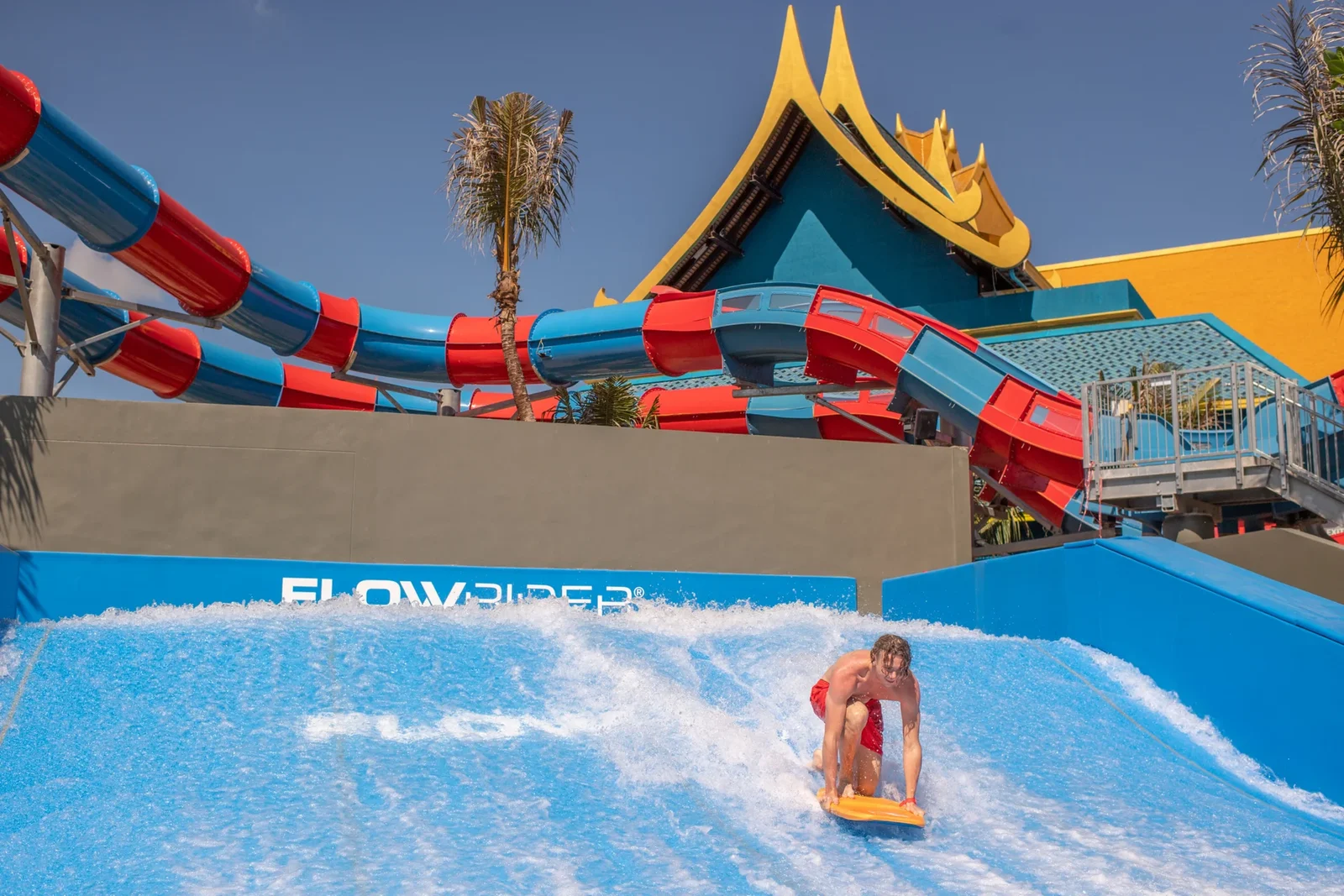 Посетитель на бодиборде катается на искусственной волне FlowRider в Андаманде перед сине-золотым зданием